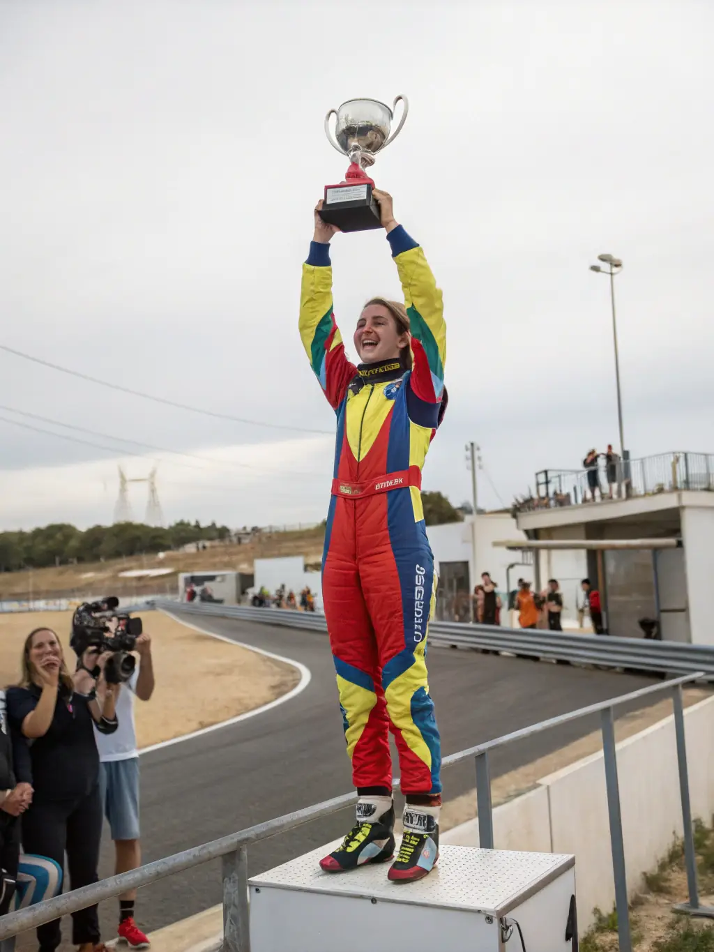 A young driver receiving a trophy and certificate at an awards ceremony, surrounded by family and mentors, celebrating their achievements in a motorsport competition.